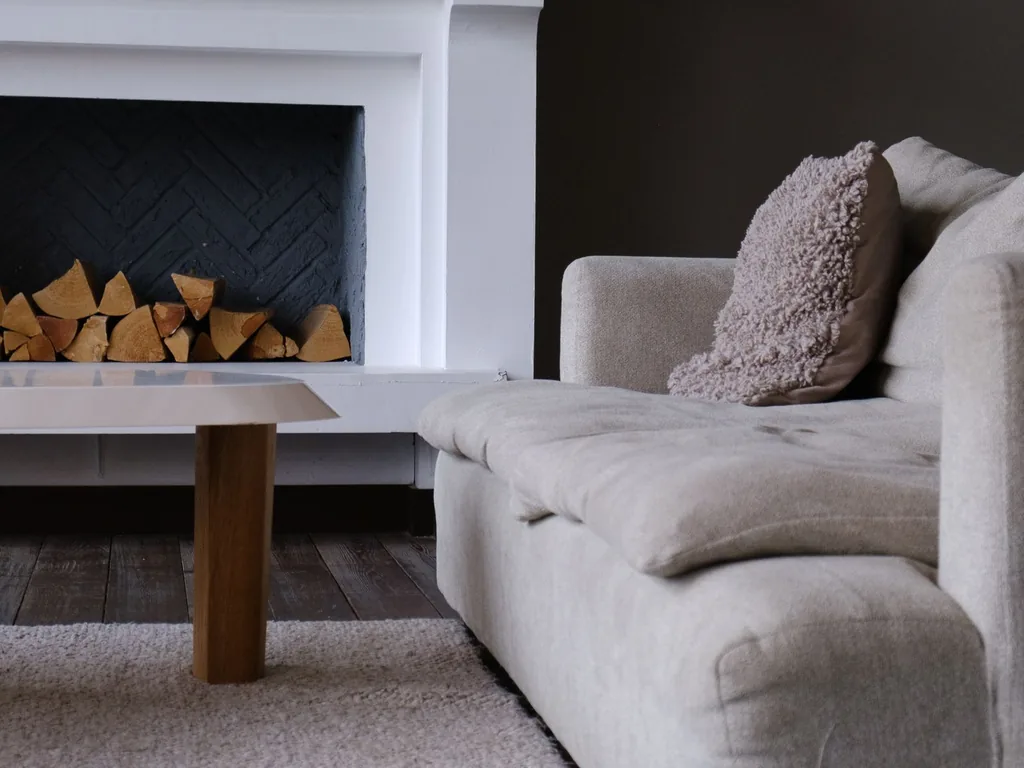 Tight close-up crop of a white plaster fireplace mantel, herringbone-tile firebox, and sofa arm before AI room redesign